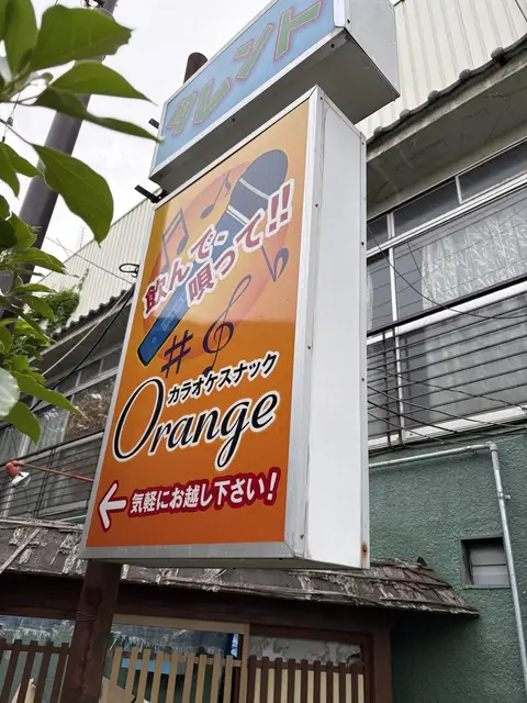 オレンジ色の縦看板に音符を散らした「カラオケスナック Orange」