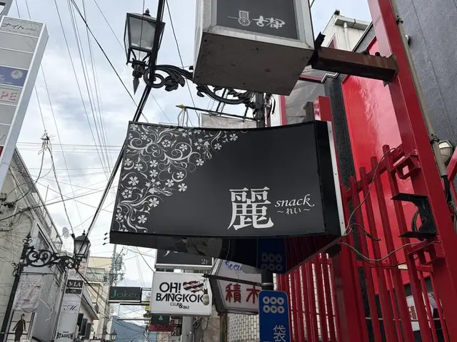 黒い袖看板に白い花模様を添えた「麗 snack」看板