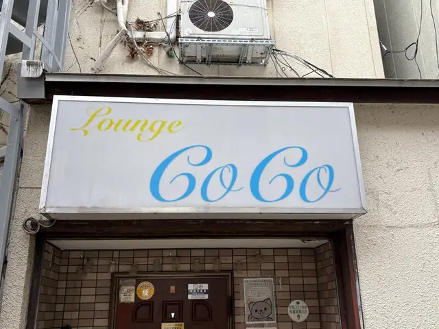 白地に水色の筆記体を置いた「Lounge CoCo」看板