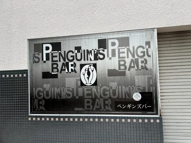 モノクロ調の面板に反復文字を重ねた「PENGUIN’S BAR」看板