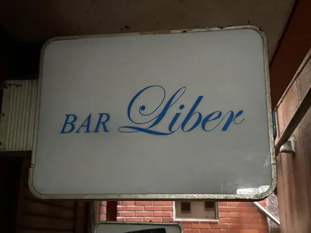 白い面板に青い筆記体を置いた「BAR Liber」看板