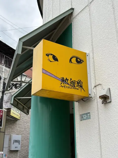 白い外壁から突き出す黄色い「熱視線」袖看板