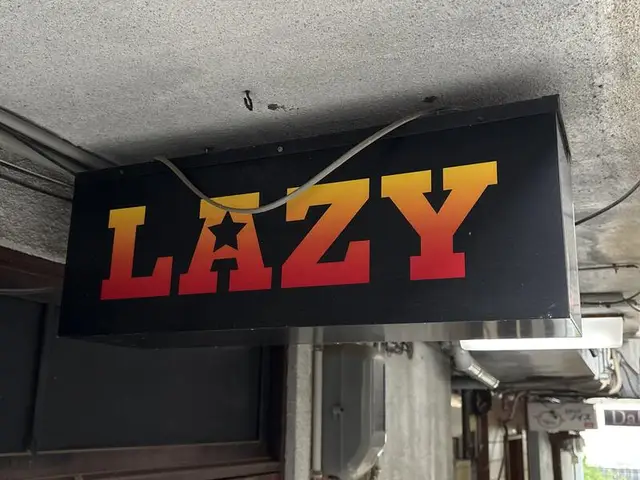 黒地に赤黄文字の「LAZY」看板