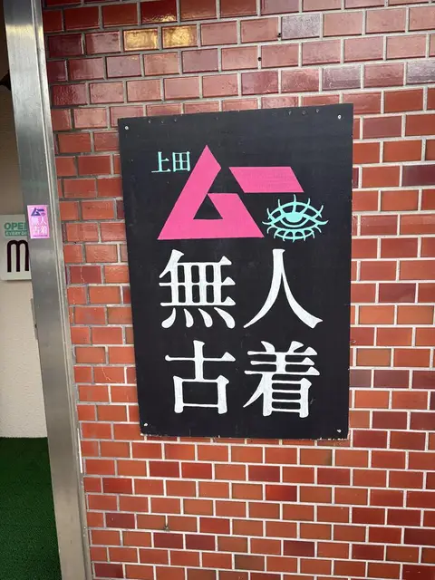 上田の煉瓦壁に掛かった『無人古着』の黒地ロゴ看板